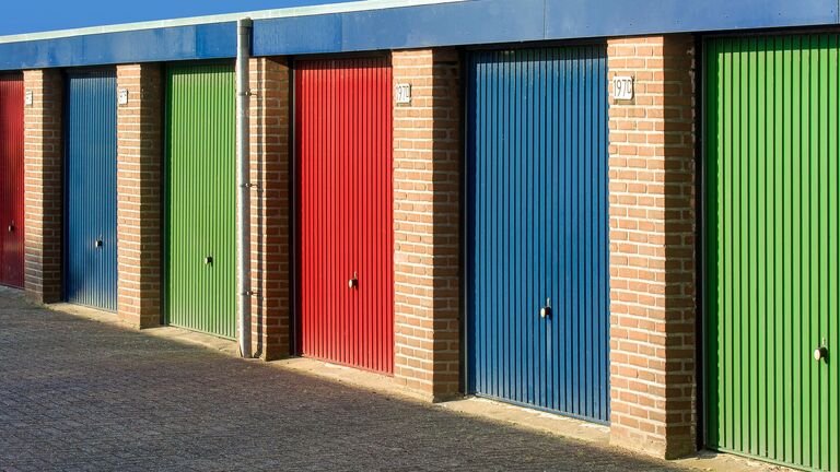 Fila de boxes con puertas metálicas de colores en un edificio bajo de ladrillo, a pleno sol