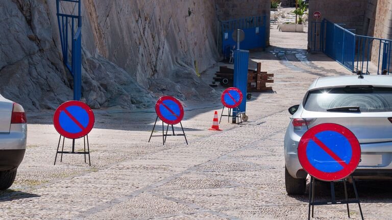 Señales portátiles de prohibido aparcar colocadas sobre una calle empedrada junto a coches aparcados