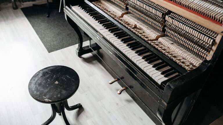 Piano vertical negro con la tapa abierta y la mecánica a la vista junto a una banqueta redonda de madera